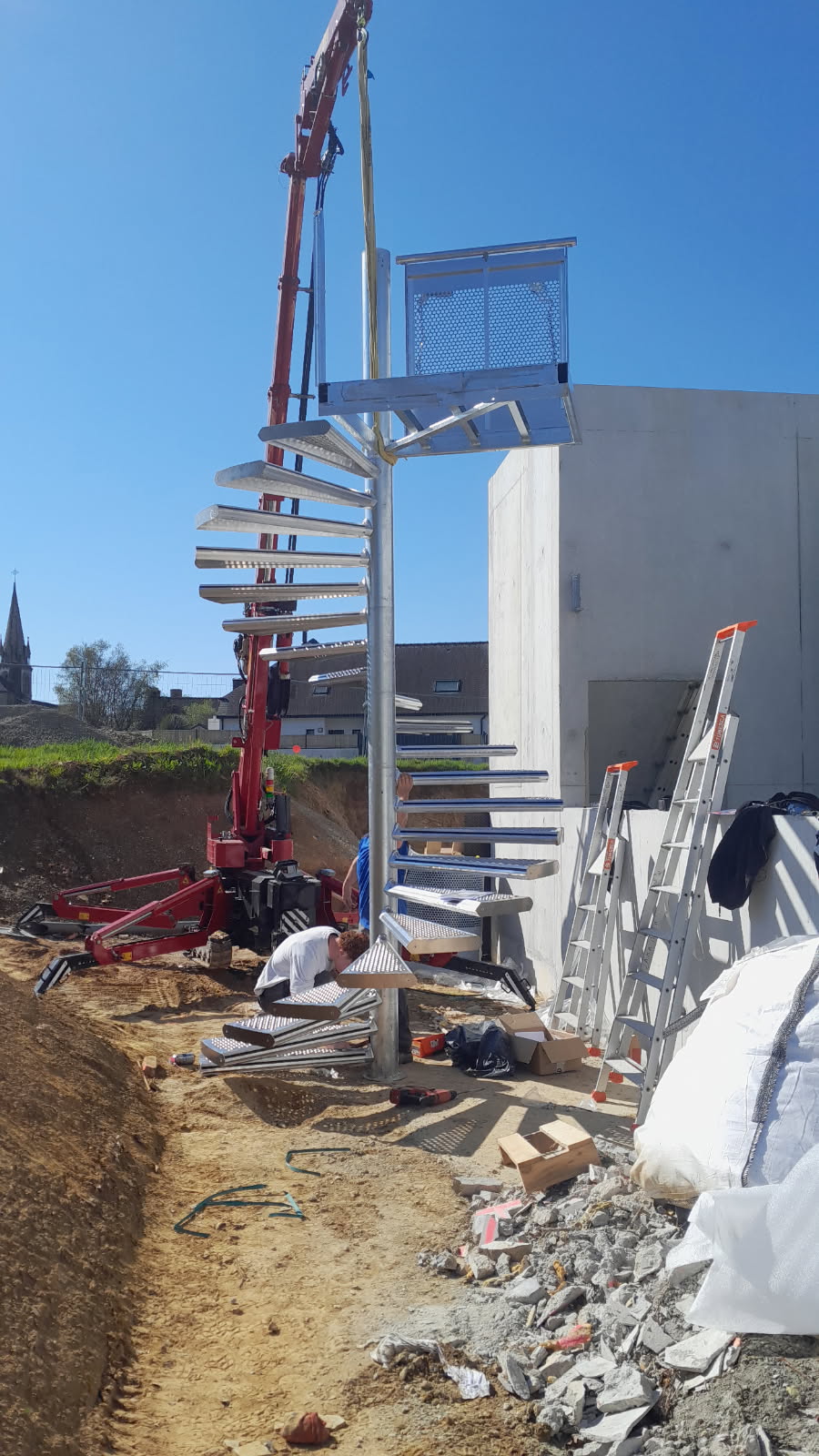 Installation d’un escalier en colimaçon métallique sur un chantier extérieur à l’aide d’une grue.